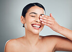 A beautiful young mixed race woman with glowing skin posing against grey copyspace background. Hispanic woman with natural looking eyelash extensions smiling while feeling her smooth skin in a studio