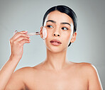 One beautiful mixed race woman using a rose quartz derma roller during a selfcare grooming routine. Young hispanic woman using anti ageing tool against grey copyspace background