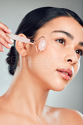 Buy stock photo Skincare, woman and rose quartz roller for glow, beauty and circulation treatment. Face, stone and model with cosmetics for facial massage, wellness benefits and dermatology on gray studio background