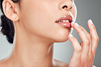 Closeup of a beautiful young mixed race woman with glowing skin posing against grey copyspace background. Hispanic woman applying lipgloss in a studio