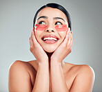 A beautiful happy mixed race woman wearing under eye patches. Hispanic model with glowing skin using hydrating treatment against a grey copyspace background