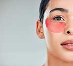 Studio closeup portrait of a beautiful mixed race woman wearing under eye patches. Hispanic model with glowing skin using hydrating treatment against a grey copyspace background