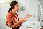 One young hispanic female call centre telemarketing agent talking on a headset while working on a computer in an office. Focused mixed race business woman consultant operating helpdesk for customer service support