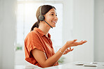 One happy young hispanic female call centre telemarketing agent talking on a headset while working on a computer in an office. Confident and friendly mixed race business woman consultant operating helpdesk for customer service support