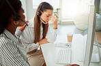 Stressed young hispanic call centre agent looking worried and suffering with headache while being comforted and consoled by a colleague in an office. Woman offering sympathy and support to frustrated and upset coworker