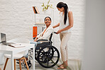 Young mixed race businesswoman helping a colleague in a wheelchair to her office at work. Hispanic businessperson with a disability being helped to her desk at work