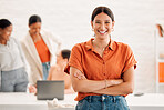 Young happy mixed race businesswoman standing with her arms crossed in an office at work. Confident cheerful hispanic businessperson standing in a meeting at work