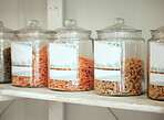 Glass jars of different types of pasta lined up in a row on a display shelf in a grocery store. Get to the local grocer for all your cooking needs. Every chef needs a variety of pasta in their kitchen