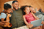 A happy mixed race family of four relaxing and lying on the lounge floor together. Loving black single parent bonding with his kids while using a digital tablet to watch movies