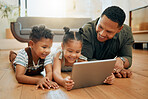 A happy mixed race family of three relaxing and lying on the lounge floor together. Loving black single parent bonding with his kids while using a digital tablet stream