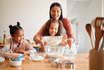 Females only, happy mixed race family of three cooking in a messy kitchen together. Loving black single parent bonding with her daughters while teaching them domestic skills at home