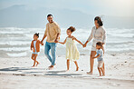 Happy mixed race family with three children holding hands and walking along the beach together. Loving parents with two daughters and son having fun and spending time while on vacation