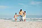 Cheerful young mixed race father running on the beach with his two daughters. Two energetic little girls enjoying day at the beach while on holiday with their dad