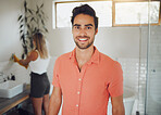 Portrait of a young caucasian couple sharing a bathroom with focus on happy young man smiling showing perfect teeth while looking at the camera in the foreground. Girlfriend washing hands in background