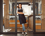 Proud businesswoman standing in the entrance of her coffeeshop. Portrait of happy small business owner standing in the door of her shop. Confident boss with her arms crossed in her restaurant