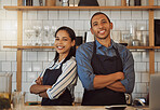 Business partners standing back to back in their coffeeshop. Restaurant colleagues standing next to each other. Portrait of two entrepreneurs arms crossed. Businesspeople in their cafe kitchen