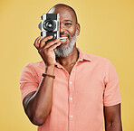 One happy African American man standing against a yellow background in a studio and taking pictures on a camera. Confident cheerful black man holding a camera and taking photographs. Smile and pose 