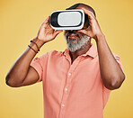 One mature african american man using a virtual reality headset while standing in studio isolated against a yellow background. Handsome man with a grey beard using wireless technology to play games