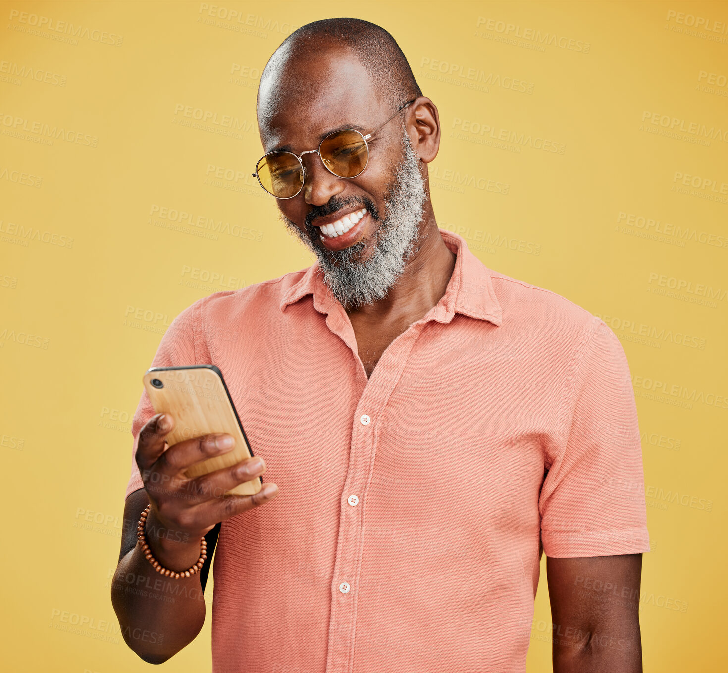 Buy stock photo Studio, phone and mature black man reading happy online chat, email or social media post with trendy fashion. Smile, smartphone and person with cool style, mobile app for text and yellow background