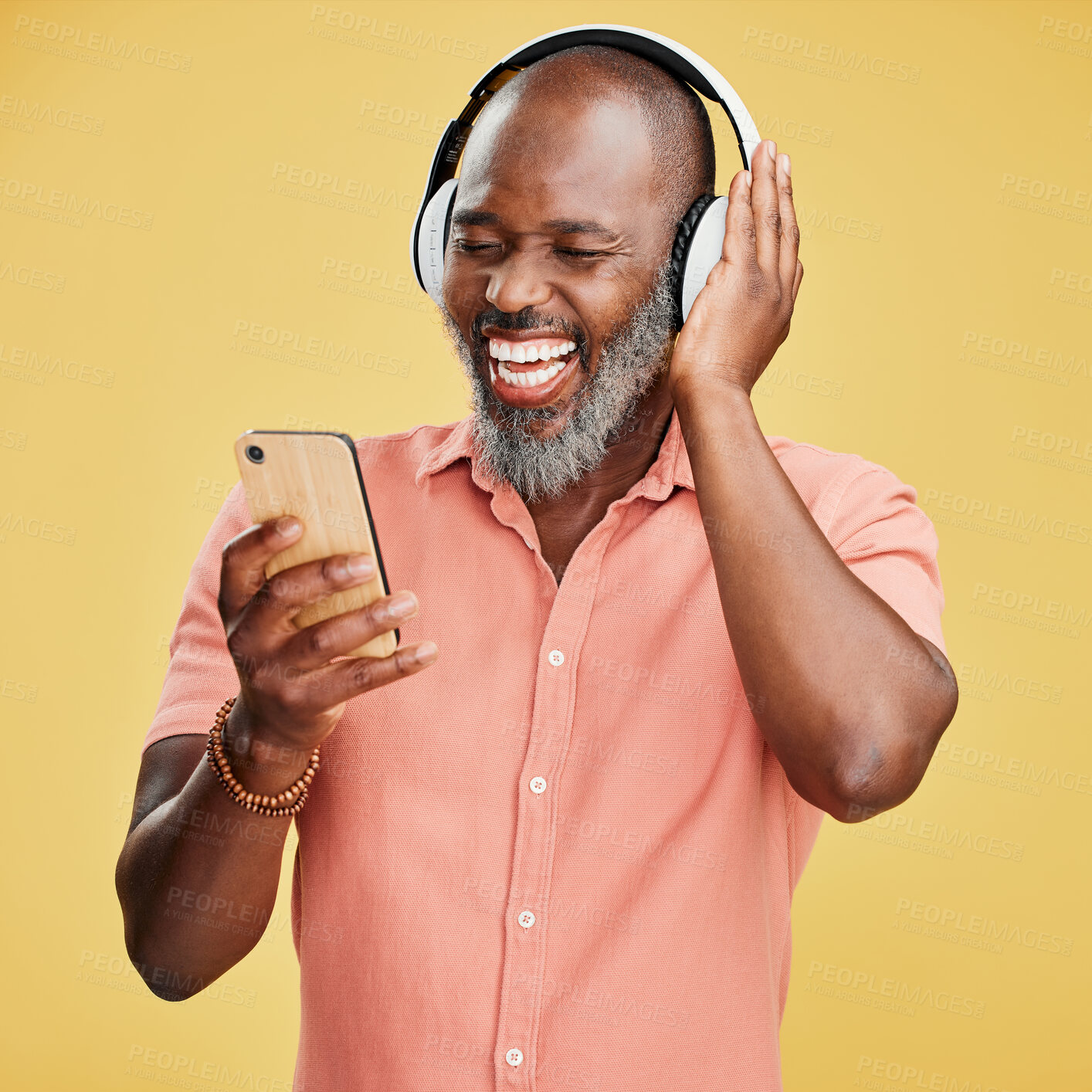 Buy stock photo Black man, headphones and phone in studio, hearing audio and streaming radio on yellow background. Mature person, energy and funny podcast for humor, search website and online for hip hop playlist