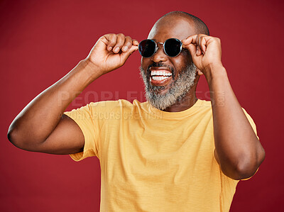 Buy stock photo Black man, fashion and laughing with sunglasses in studio for trendy style, designer eyewear or summer ready. Mature person, happy or edgy face accessory for aesthetic or confidence on red background