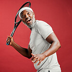 One happy mature african american man standing against a red background in studio and posing with a tennis racquet. Smiling black man feeling fit and sporty while playing a match. Ready for the court