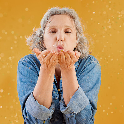 Buy stock photo Blowing, celebration and glitter with senior woman in studio isolated on yellow background for event. Birthday, confetti or retirement with mature person holding sparkling streamers for milestone