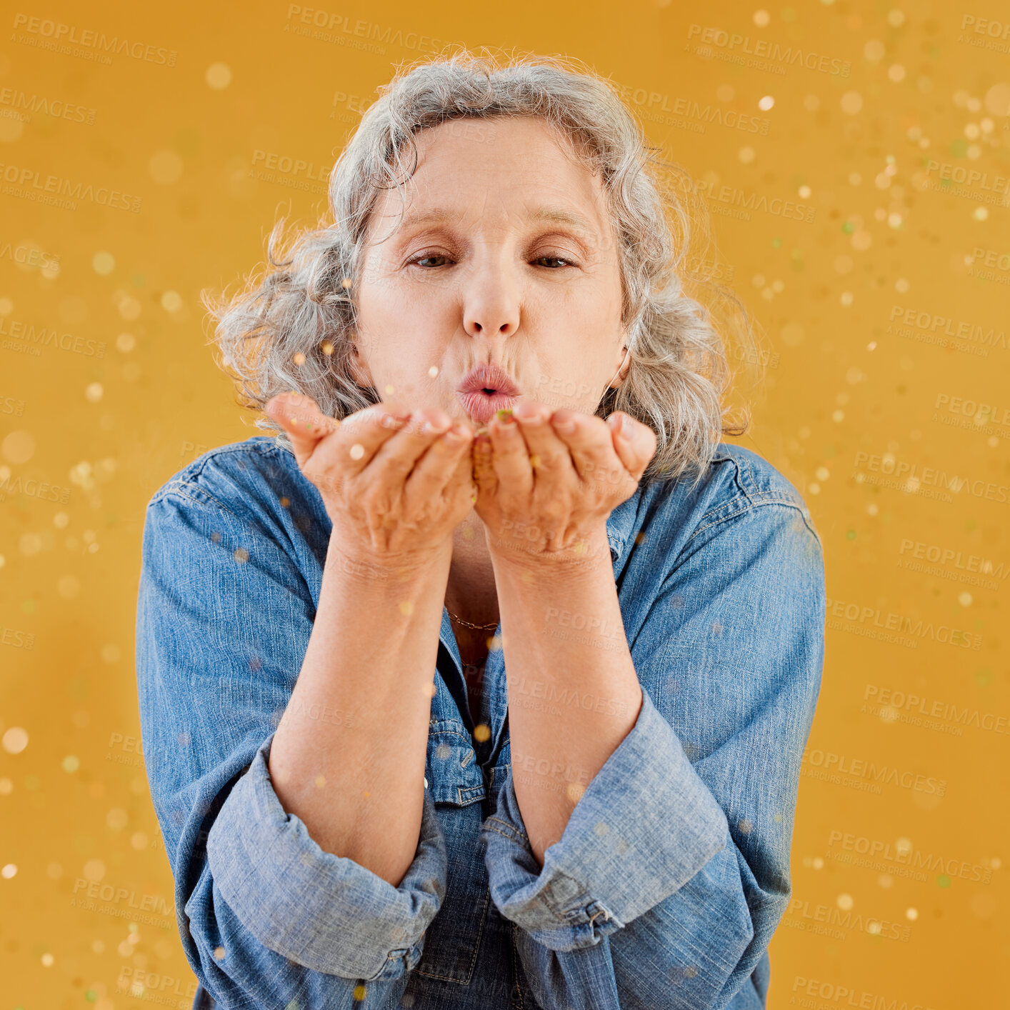 Buy stock photo Blowing, celebration and glitter with senior woman in studio isolated on yellow background for event. Birthday, confetti or retirement with mature person holding sparkling streamers for milestone