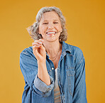 One happy mature caucasian woman playing with a sparkler on her birthday while posing against a yellow background in the studio. Smiling white lady showing joy and happiness while celebrating