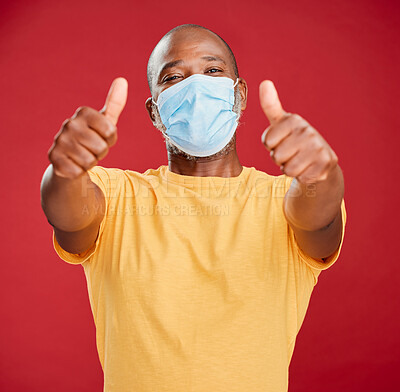 Buy stock photo Black man, portrait and mask with thumbs up for protection or good safety on a red studio background. African, male person or model with face cover, like emoji or yes sign for winning or great review