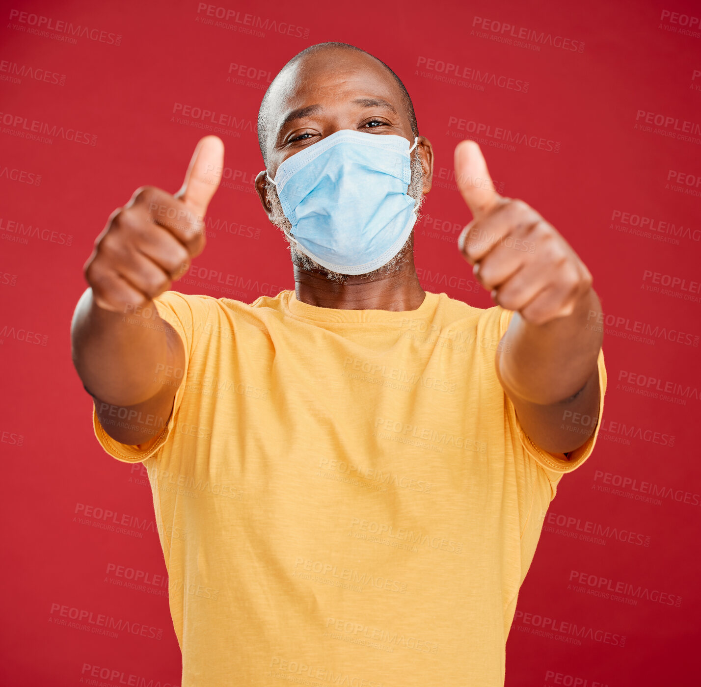 Buy stock photo Black man, portrait and mask with thumbs up for protection or good safety on a red studio background. African, male person or model with face cover, like emoji or yes sign for winning or great review