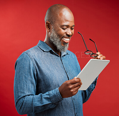 Buy stock photo Mature, black man and reading with tablet in studio for ebook or social media on a red background. African, male person or model with smile or glasses on technology for online browsing, app or news