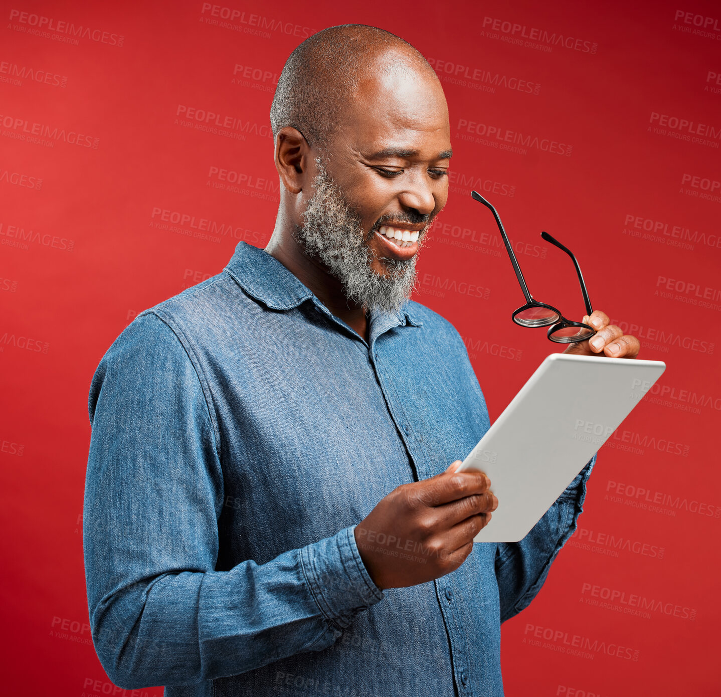 Buy stock photo Mature, black man and reading with tablet in studio for ebook or social media on a red background. African, male person or model with smile or glasses on technology for online browsing, app or news