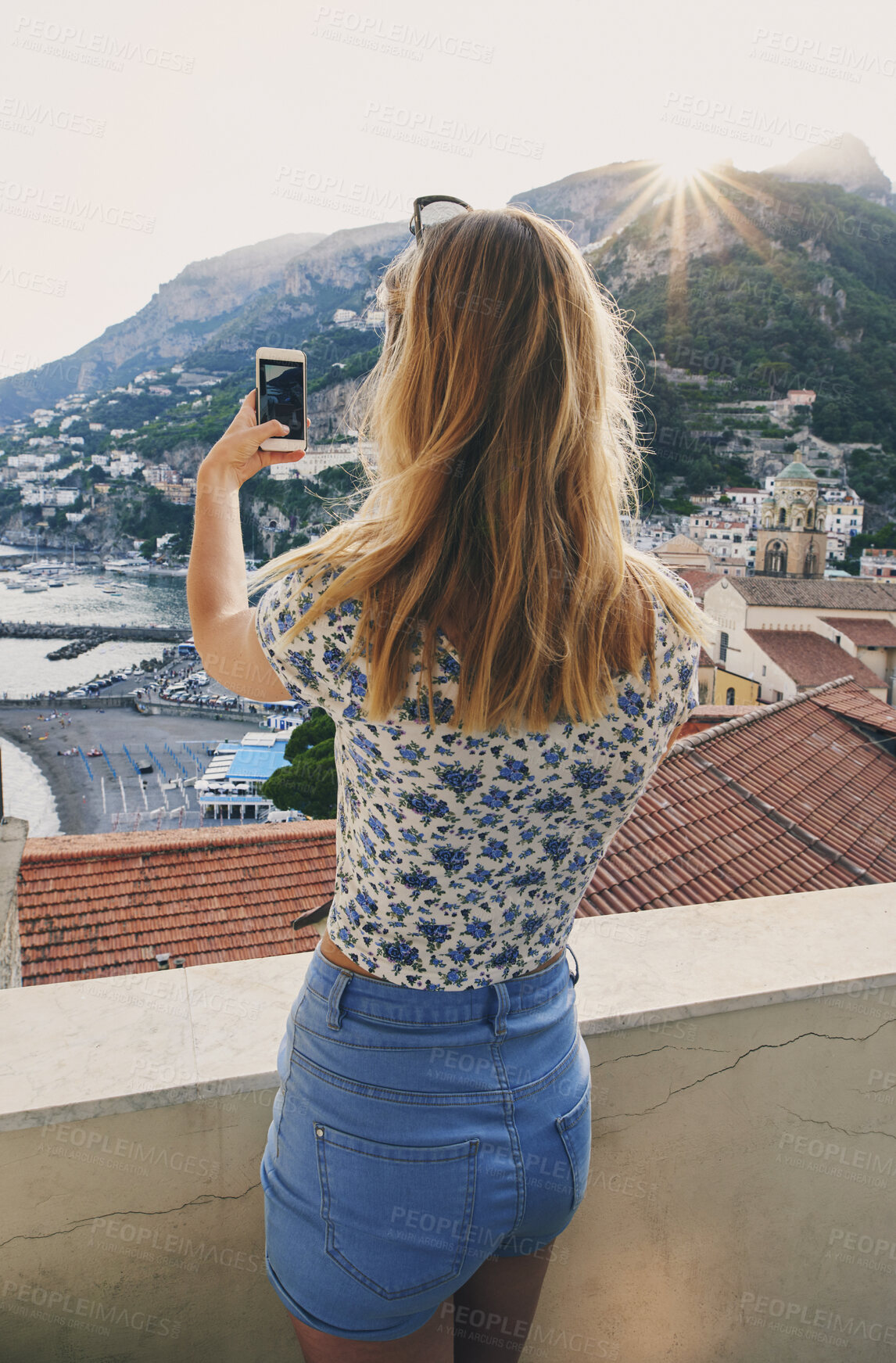 Buy stock photo Woman, phone and photography on vacation with city, ocean and mountains in morning at sunset on balcony. Person, back and outdoor with smartphone, memory and view of hills, sea and buildings in Italy