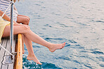 Legs of two women hanging from the side of a boat during holiday cruise. Two friends on holiday together with legs hanging over the side of the boat over the water