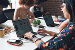 A young businesswoman working on her laptop in her office with her colleagues. A young businesswoman wearing glasses typing on her laptop in an office with a diverse group of colleagues.