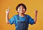 Adorable little boy looking cheerful wearing casual clothes and pointing his finger up against an orange copyspace  background. Little boy with an idea while having fun