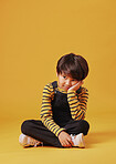 One asian boy looking sad and depressed while sitting on the floor and posing against orange copyspace background. Cute mixed race child with ADD looking bored and depressed