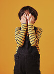 A cute little Chinese boy hiding his face while playing a game and posing against an orange copyspace background. Mixed race child with autism, avoiding and hiding his face