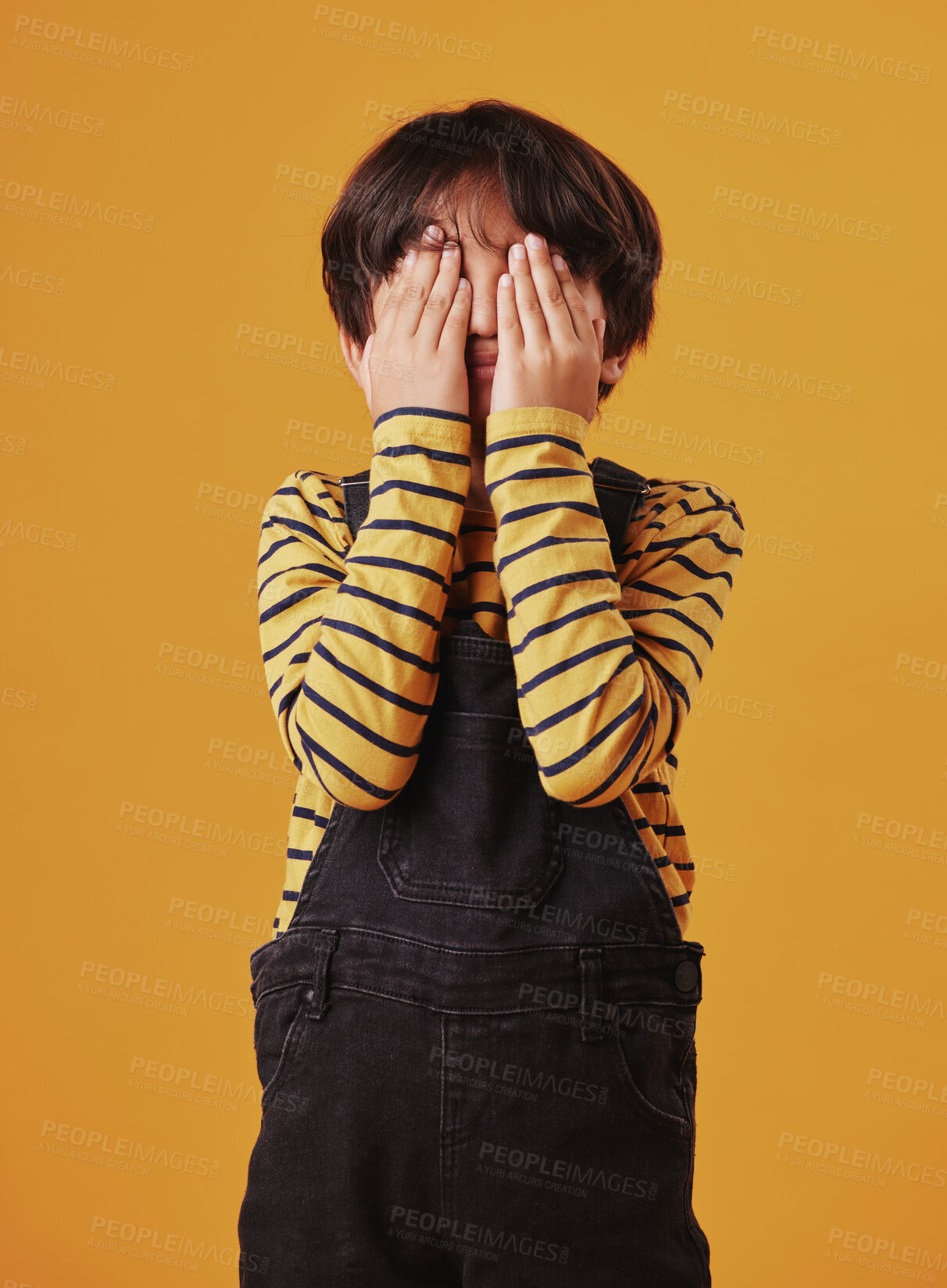 Buy stock photo Hands, peekaboo or shy with child on yellow background, isolated in studio for playing games. Fail, hide and seek or mistake with boy or fashionable kid in stripes for blame, guilt or shame