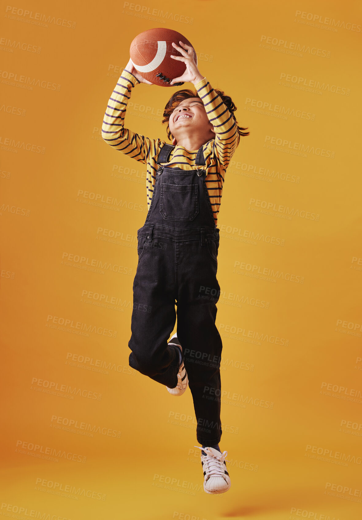 Buy stock photo Child, jump and catch football for sport, fun game and training for exercise isolated on studio background. Happy kid, air and boy with ball with energy for play, RUGBY and fitness for competition