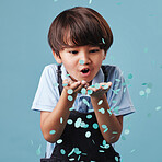 An adorable asian little boy having fun while blowing blue confetti at a gender reveal party.  Cute mixed race child being curious and playful in a studio