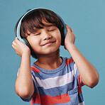 A cute young asian boy enjoying listening to music from his wireless headphones. Adorable Chinese kid smiling and feeling the magic of music while posing against an blue studio background