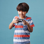 Young mixed race boy standing and holding a console controller while playing a video game against a blue background. Fun and games are a good activity for weekends