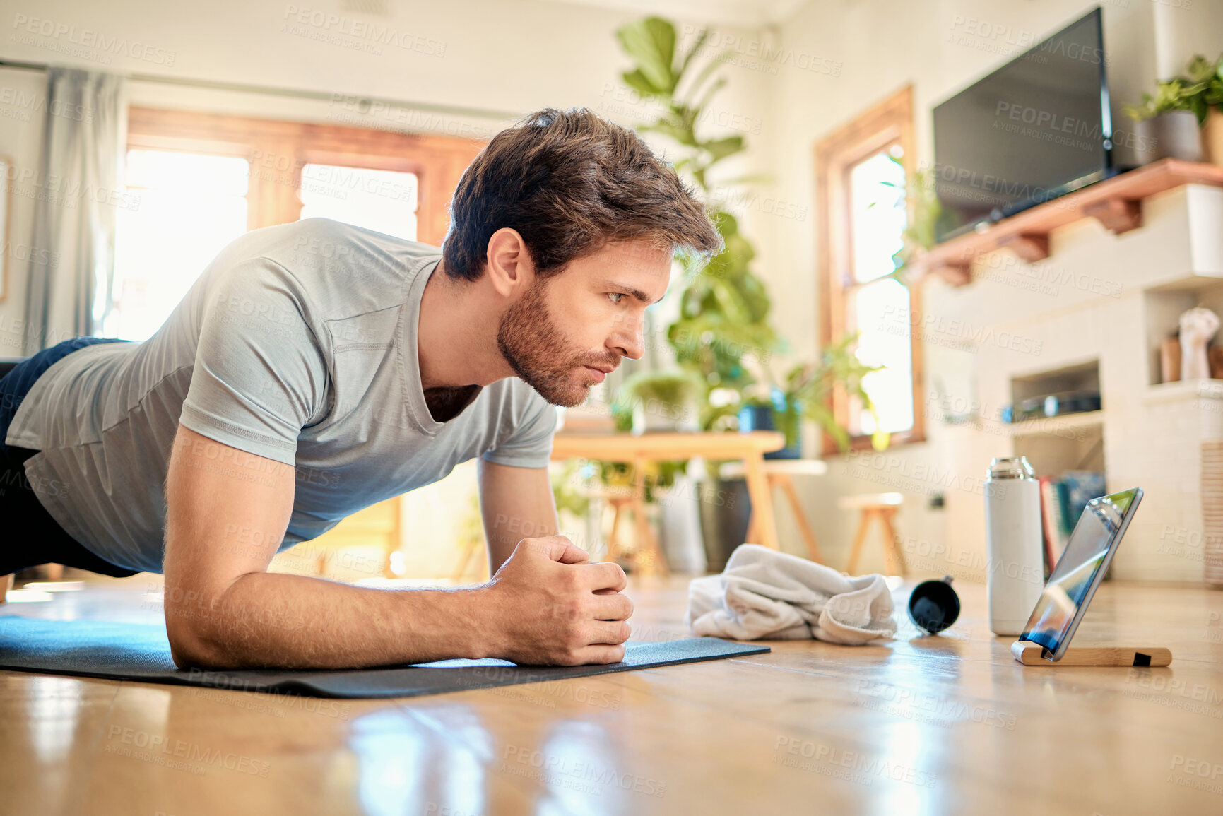 Buy stock photo One fit young caucasian man doing elbow plank hold bodyweight exercise while training with online tutorial on digital tablet at home. Focused guy gaining muscle, increase endurance, enhance upper body and core strength during workout