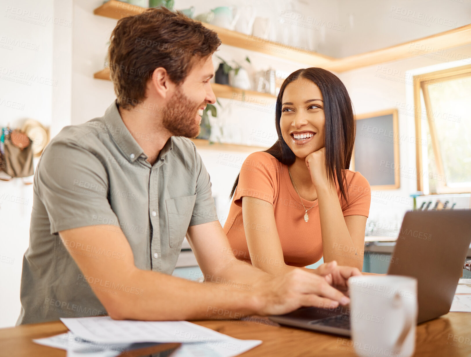 Buy stock photo Young happy interracial couple bonding while going through paper and using a laptop together at home. Caucasian boyfriend and girlfriend working through their bills and typing on a laptop. Cheerful husband and wife working on a computer together