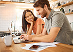 Young cheerful interracial couple bonding while working on a laptop together at home. Caucasian boyfriend and girlfriend working through their bills and using a laptop. Content wife staring at her husband while typing on a computer