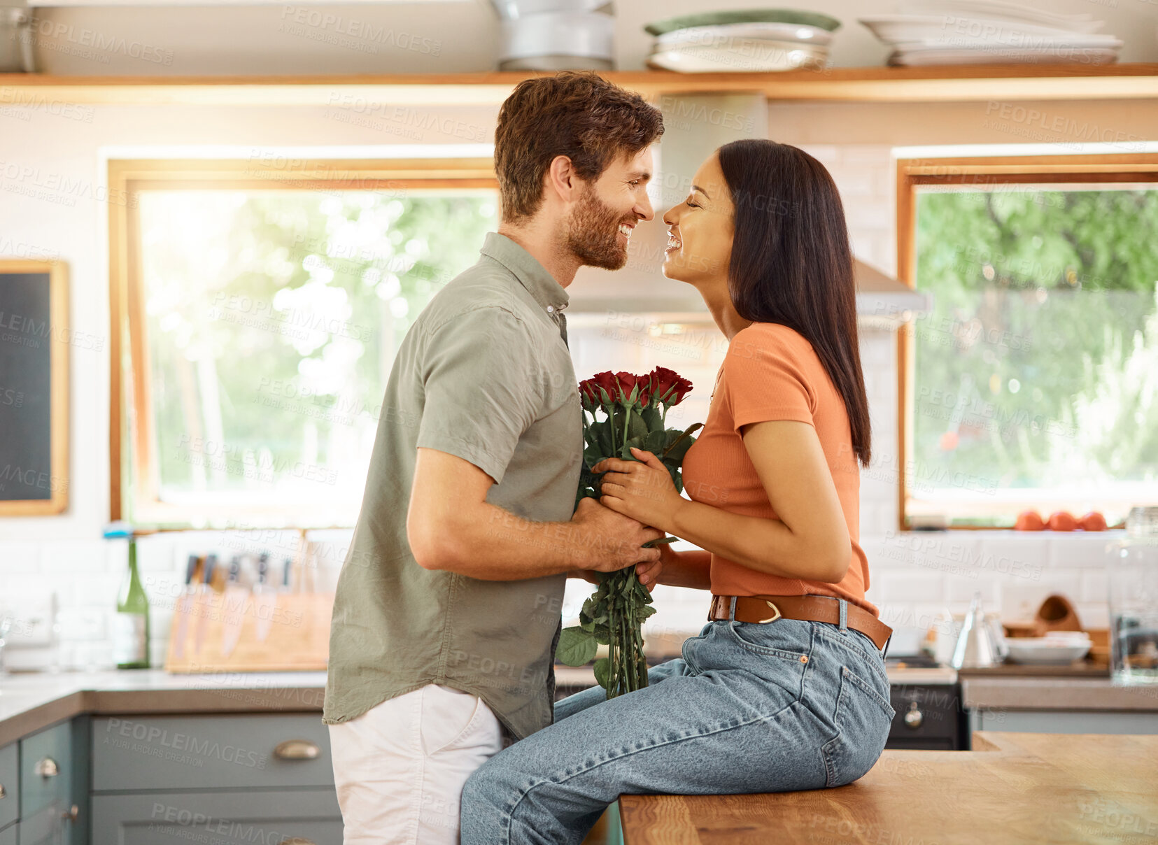 Buy stock photo Young content caucasian boyfriend giving his cheerful mixed race girlfriend a bouquet of flowers at home. Happy hispanic wife receiving roses from her husband. Interracial couple bonding together at home