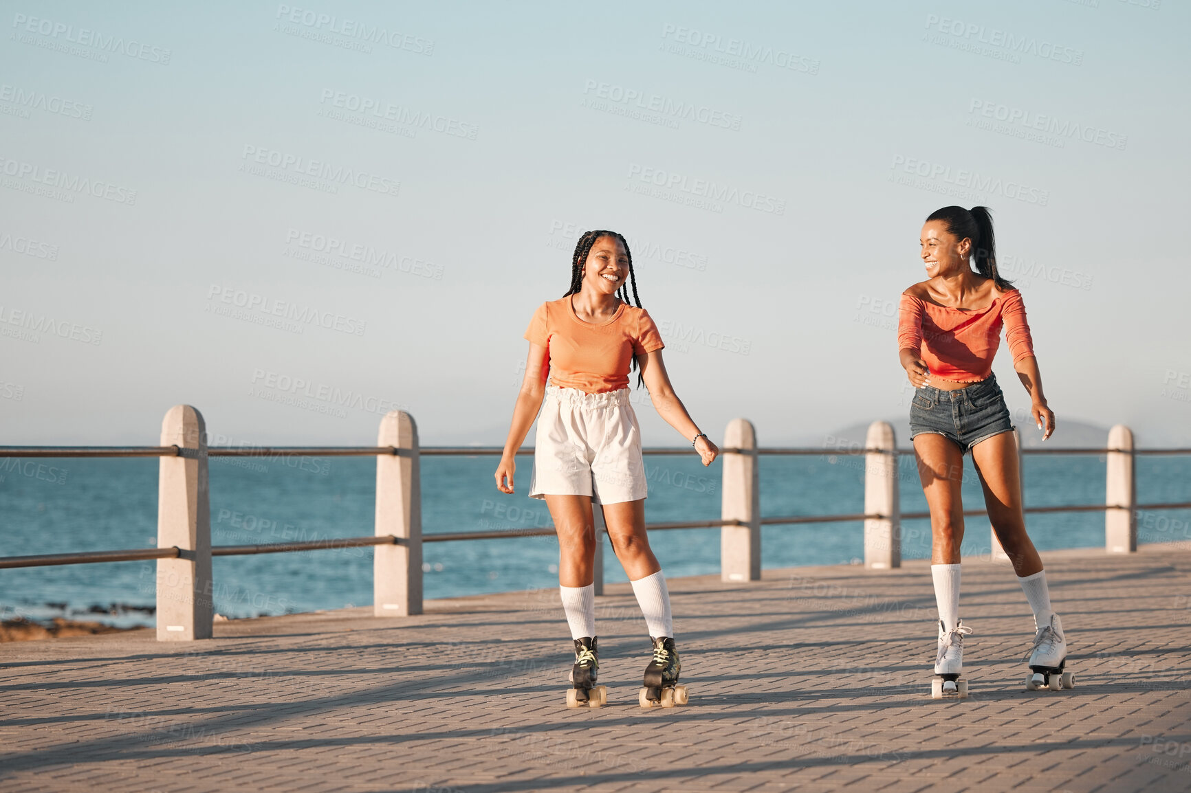 Buy stock photo Friends roller skating on the promenade at the beach during a summer vacation in South Africa. Happy, active and young girls doing a fun activity in nature on the ocean boardwalk while on holiday.