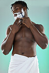 Black man shaving facial hair, skincare cream on studio background and white towel on waist. Happy young model grooming in bathroom, hygiene product and cleaning beard with cosmetic morning routine